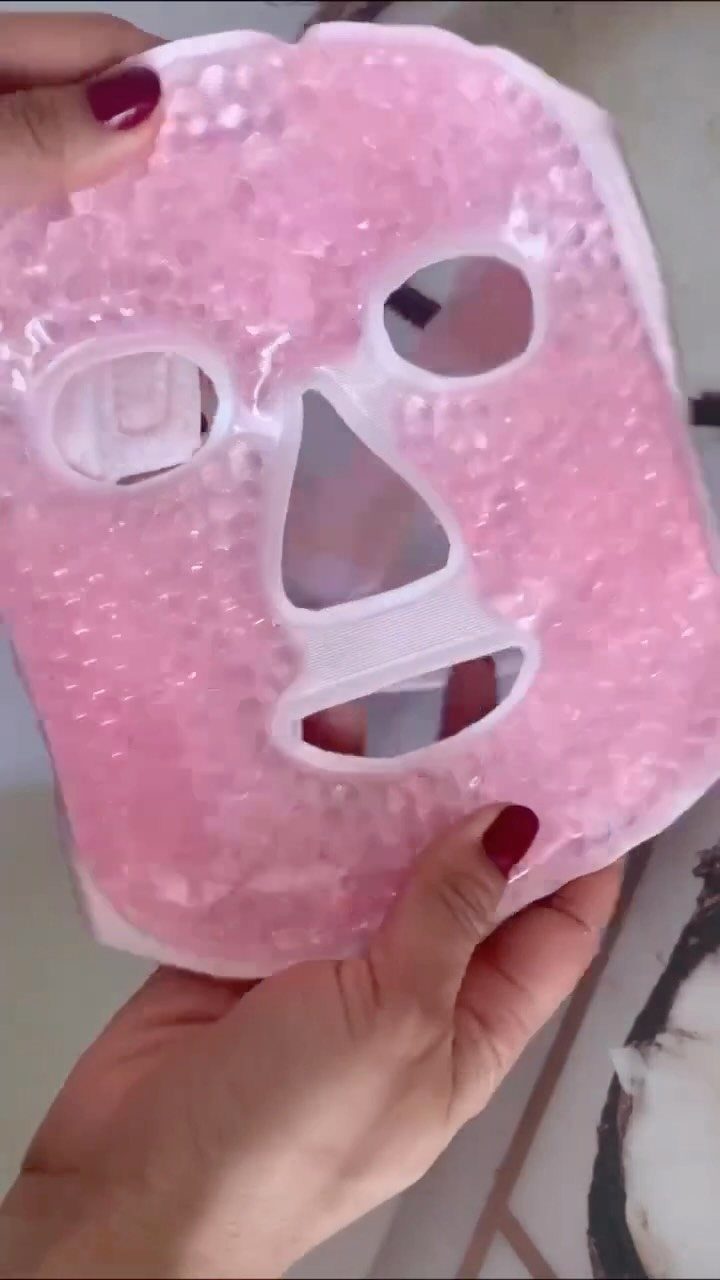 Pink gel cooling face mask held by a person with red nails.