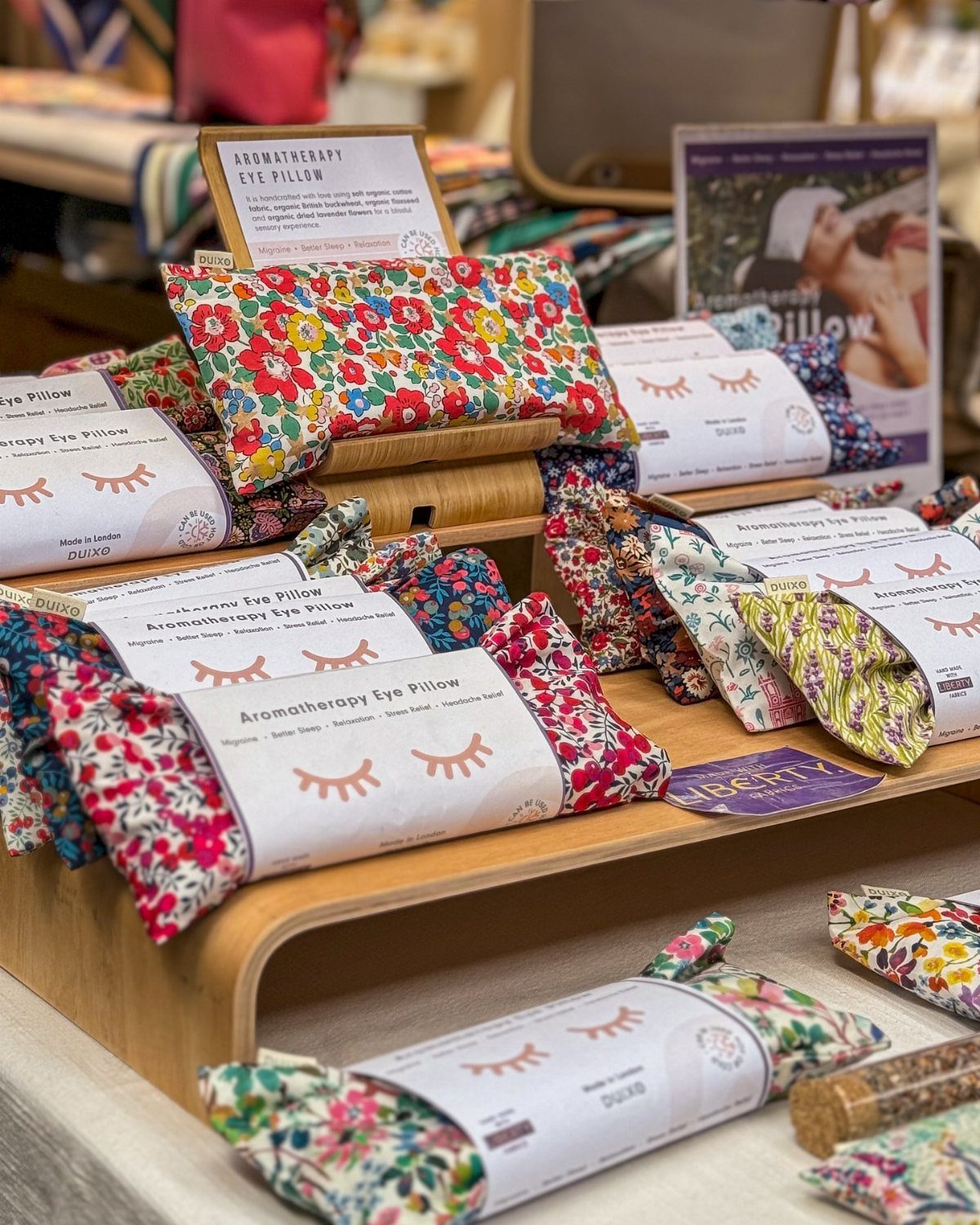 Floral aromatherapy eye pillows displayed on wooden shelves with descriptive product labels.