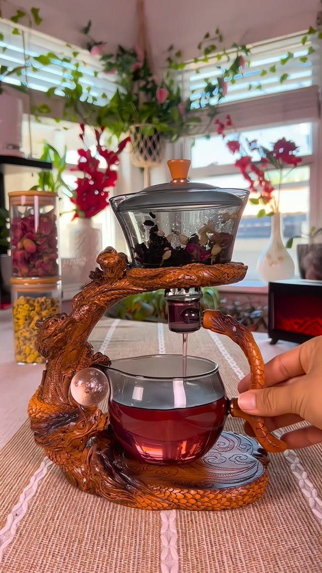 Decorative tree-branch tea set brewing red tea into a glass cup.