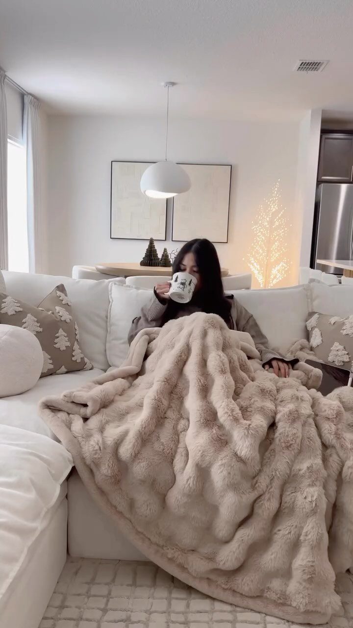 Woman wrapped in a beige textured throw blanket sitting on a white sofa.