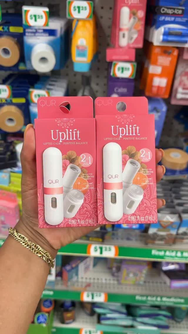 Two pink Uplift aromatherapy inhaler packages held in a hand at a store.