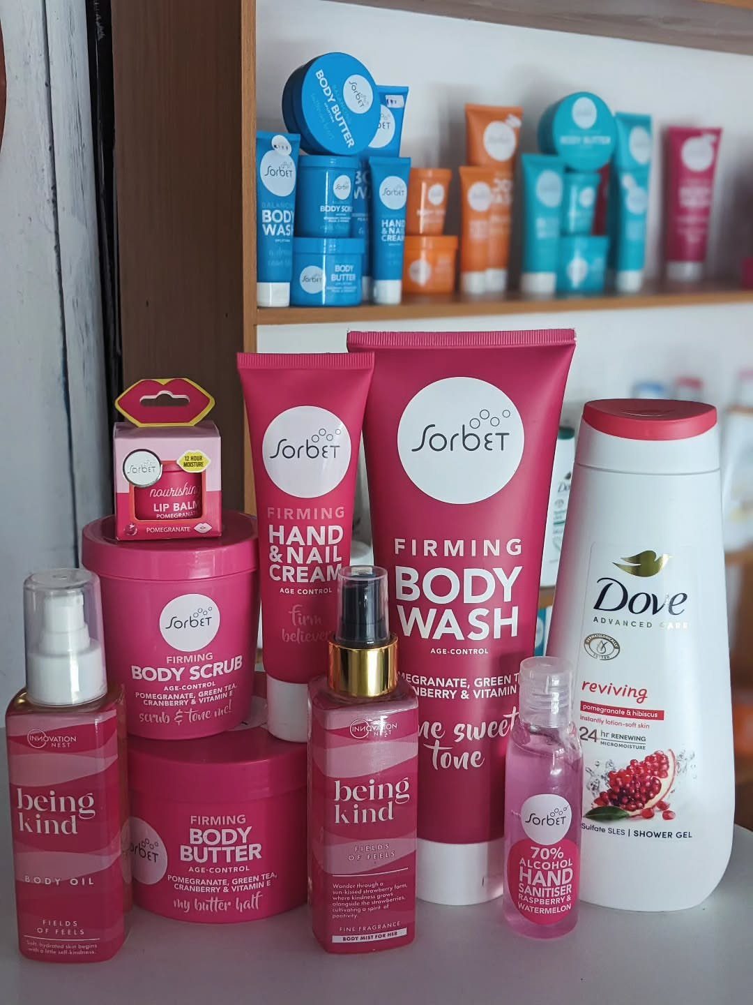 Assorted pink and white skincare bottles and jars arranged on a wooden shelf.