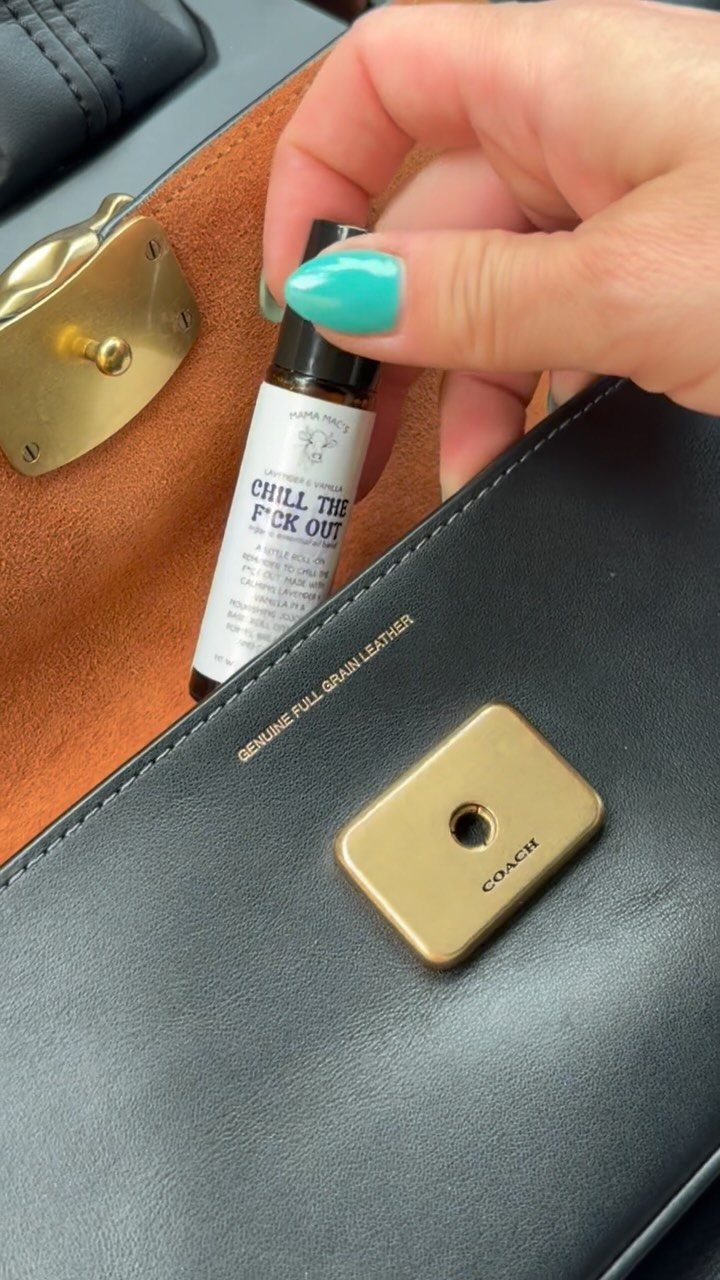 Small brown essential oil bottle held inside a black leather Coach handbag.
