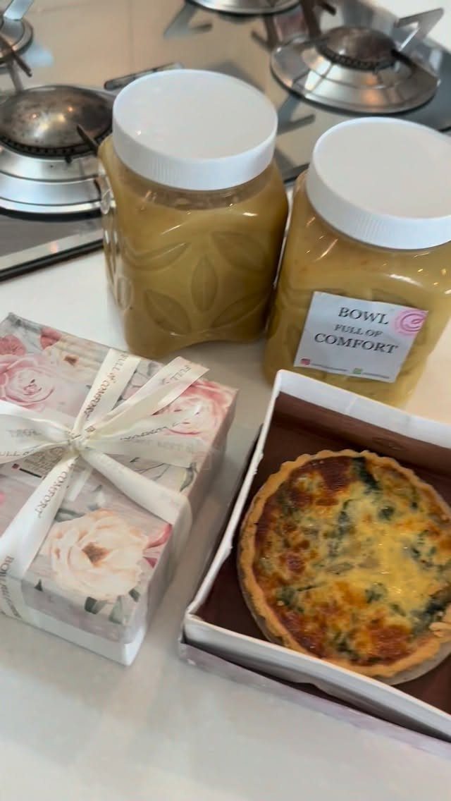Two jars of soup, a floral gift box, and a quiche on a counter.