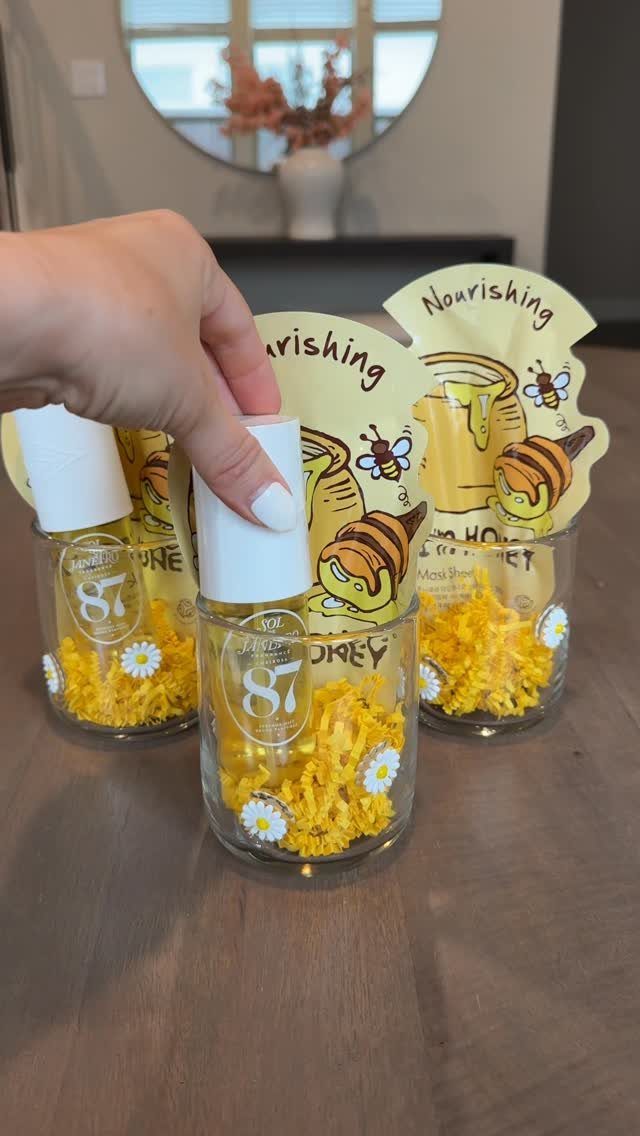 Small glass gift jars with yellow filler and honey-themed tags on a wooden table.
