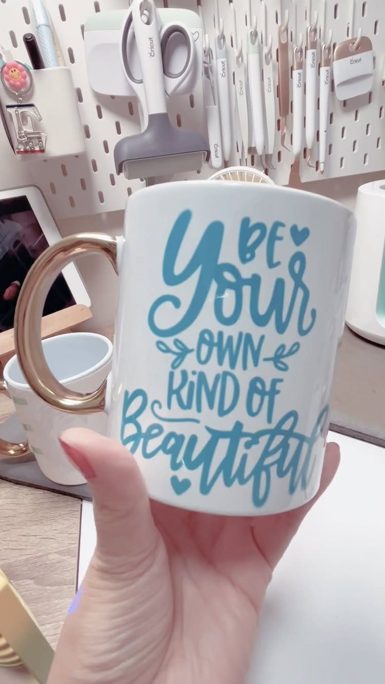 White ceramic mug with gold handle and blue self-love affirmation text held by hand.