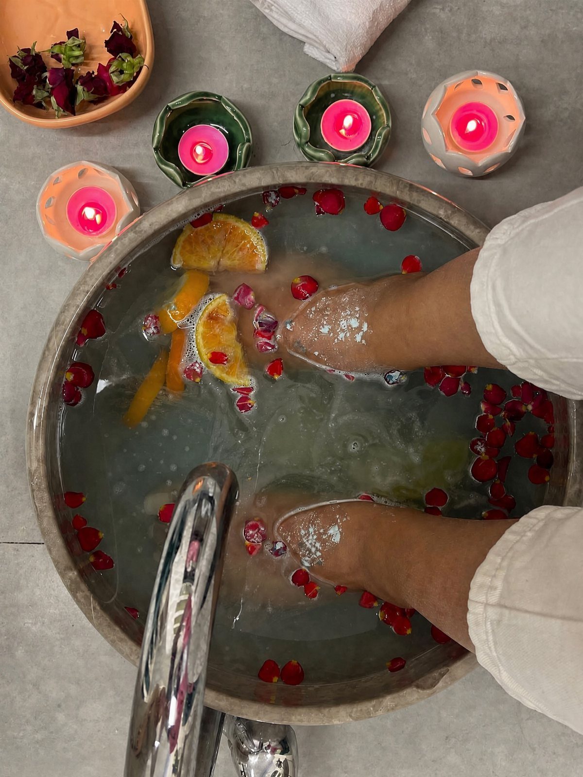 Feet soaking in a basin with orange slices, flower petals, and lit candles.