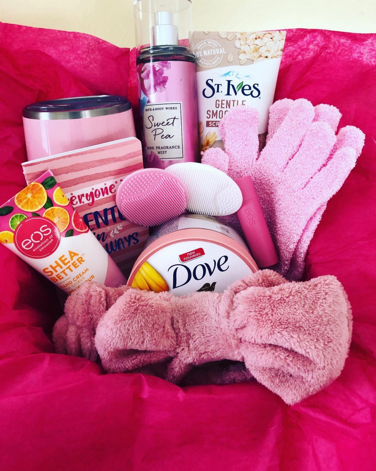 Beauty gift basket with pink skincare products, a headband, and exfoliating gloves.