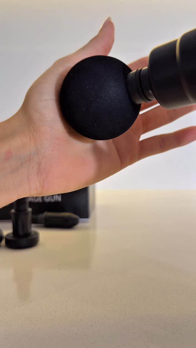 Hand being massaged by a black electric massage gun on a white surface