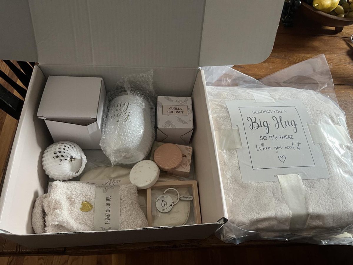 White gift box containing a cozy blanket, mug, candle, and a Big Hug card.