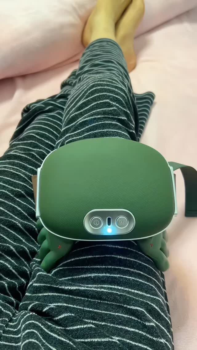 Green electronic leg massager wrapped around a person's leg in striped pajamas.