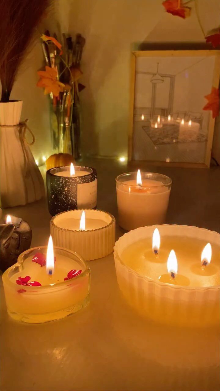 Lit scented candles of various shapes and sizes on a table with warm lighting.