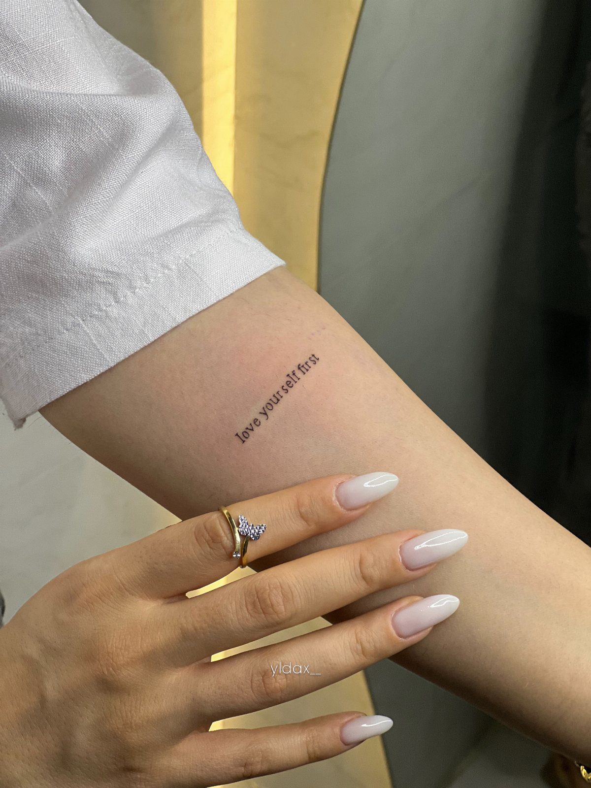 Forearm with a small black tattoo saying love yourself first and manicured hand.
