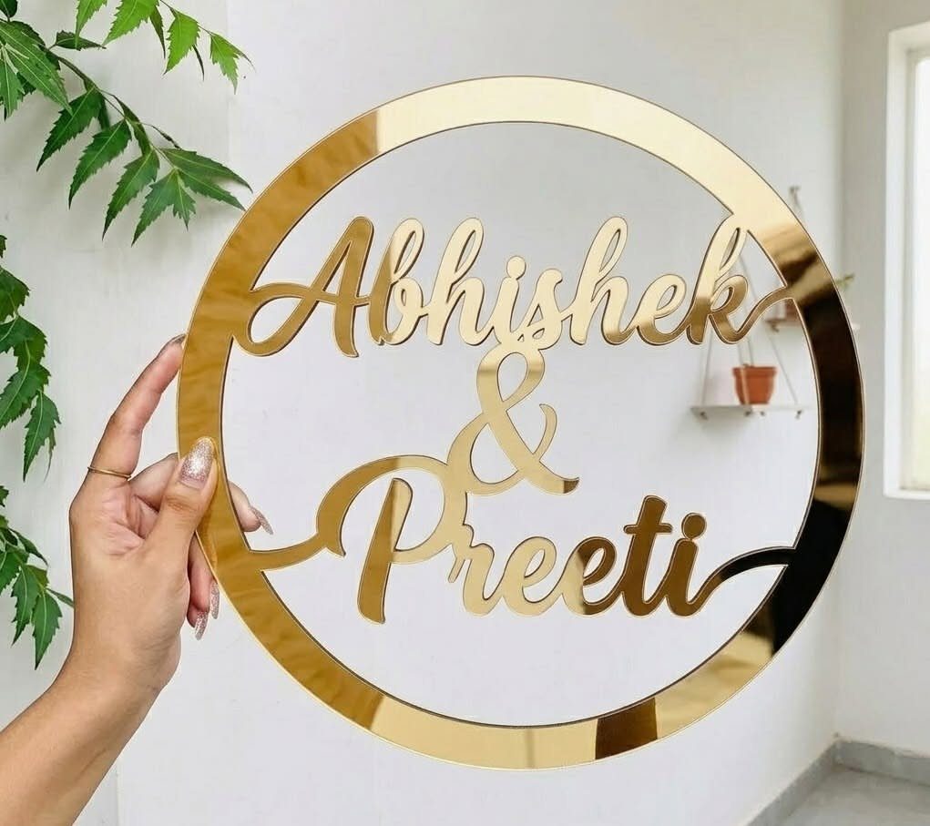 Gold mirrored acrylic circular wedding sign with names Abhishek and Preeti in cursive.