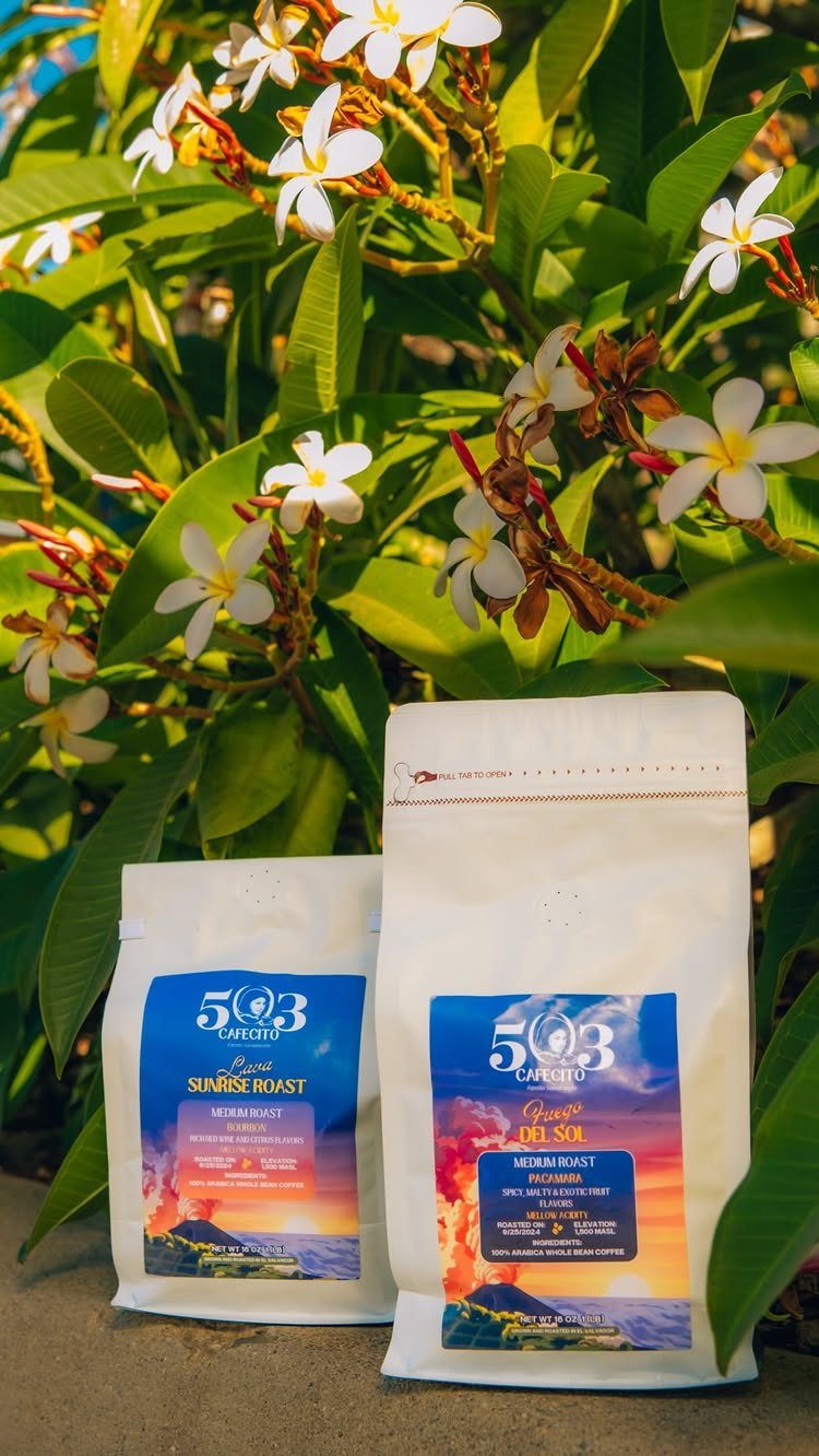 Two white bags of specialty coffee roast placed before white plumeria flowers.