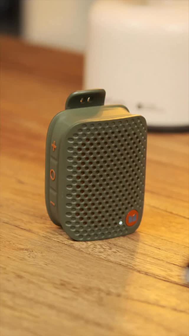 Small olive green portable speaker resting on a light wooden table surface.