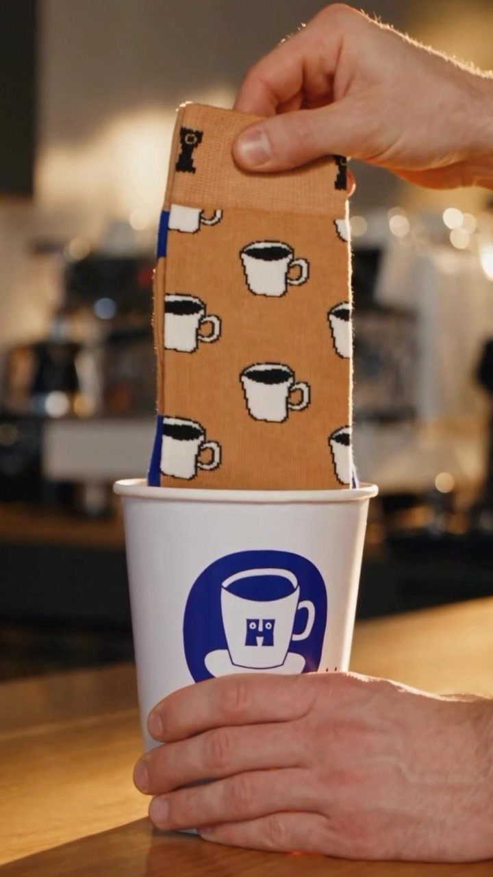 Tan coffee-patterned socks being pulled out of a white paper coffee cup