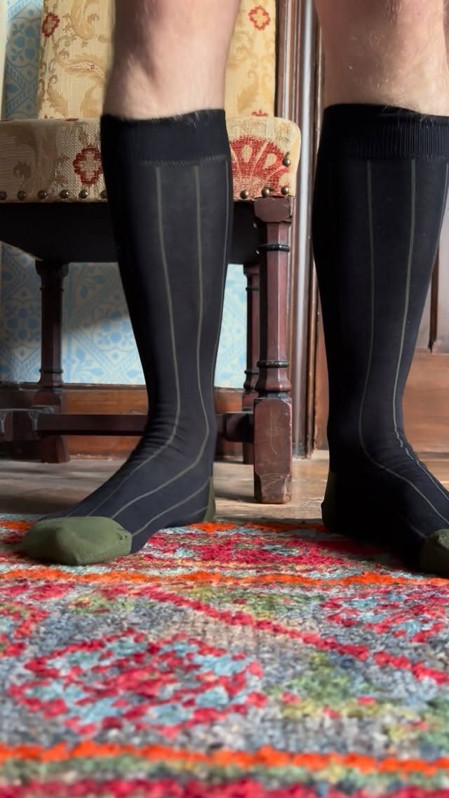 Black knee-high socks with green toes worn by a person on a colorful rug.