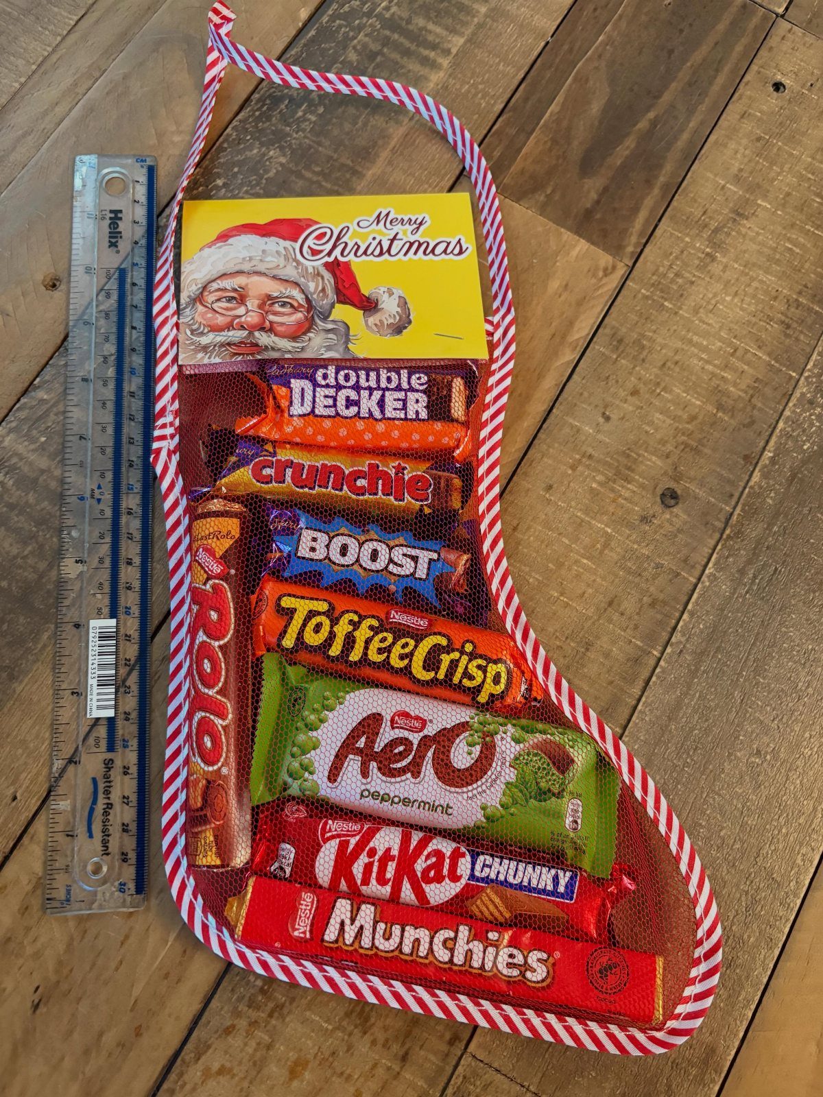 Christmas stocking filled with assorted chocolate bars and a Santa card on wood.