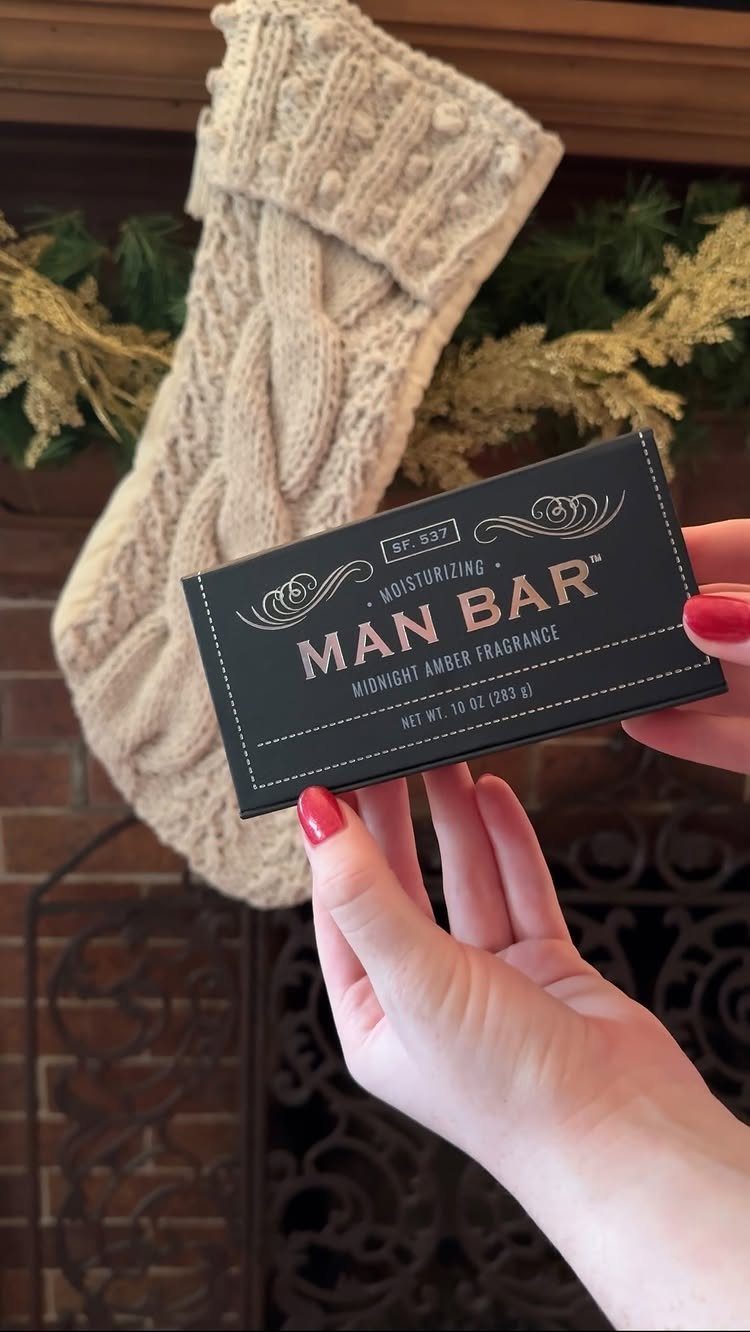 Hands holding a black Man Bar soap box in front of a Christmas stocking.