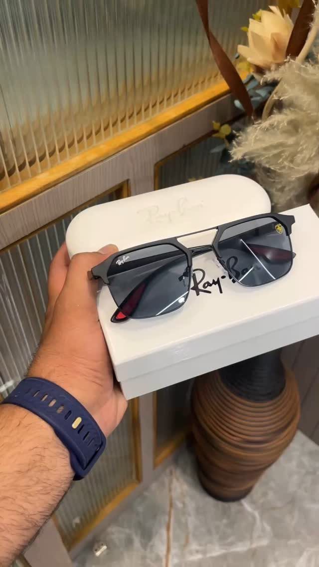 Black Ray-Ban sunglasses held over a white case by a person's hand.