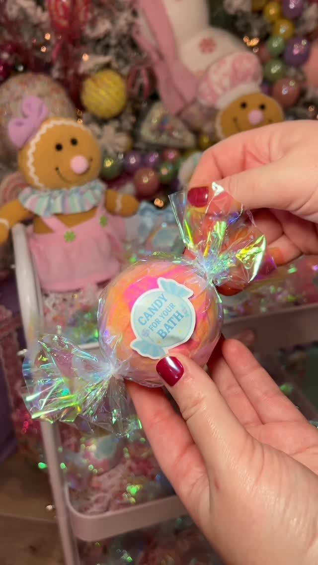 Colorful bath bomb wrapped in iridescent cellophane held by hands with red nails.
