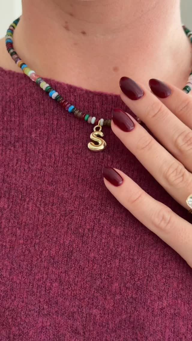 Colorful beaded necklace with a gold letter S pendant worn on a maroon sweater