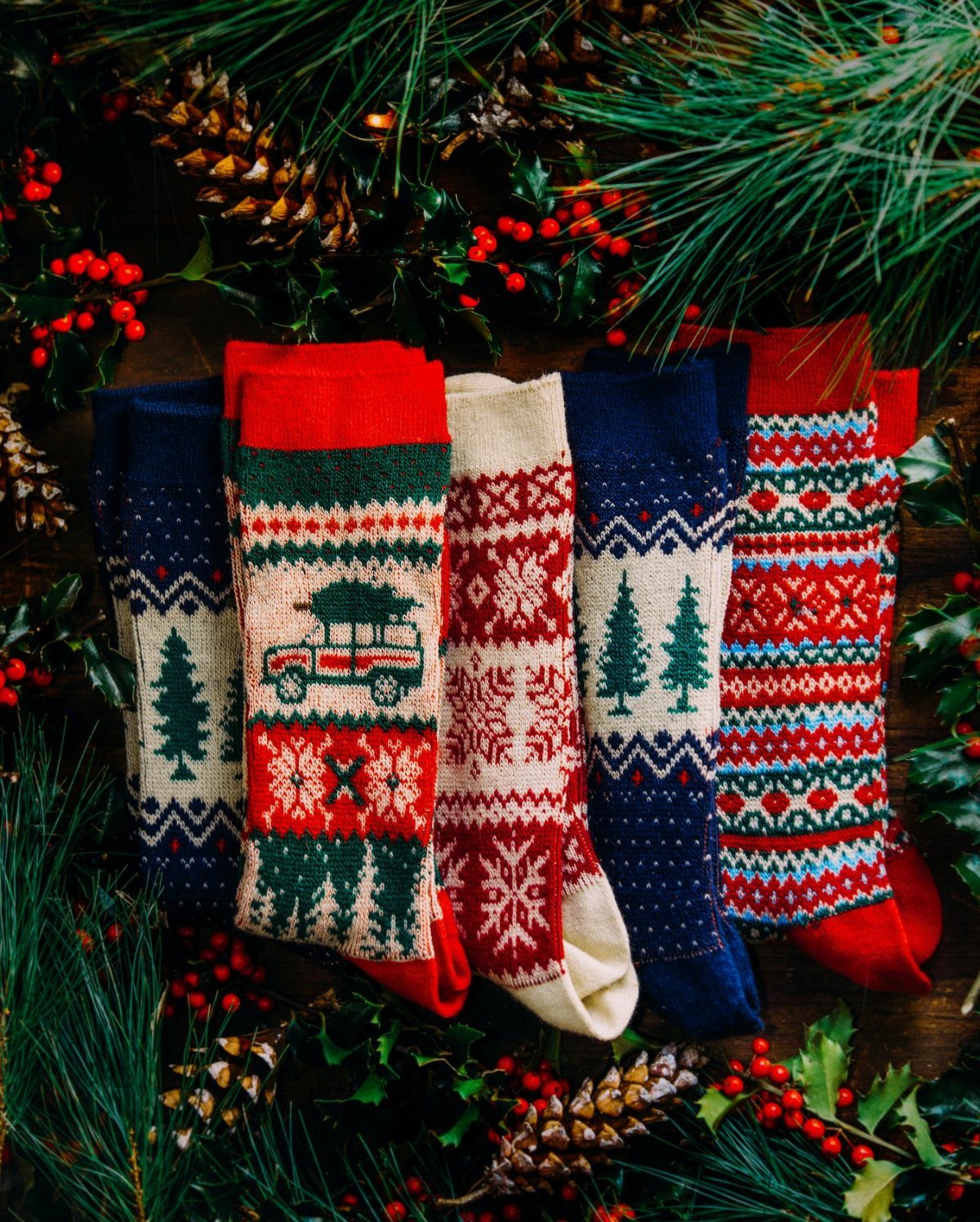 Festive knit socks with winter patterns surrounded by pine needles and red berries.