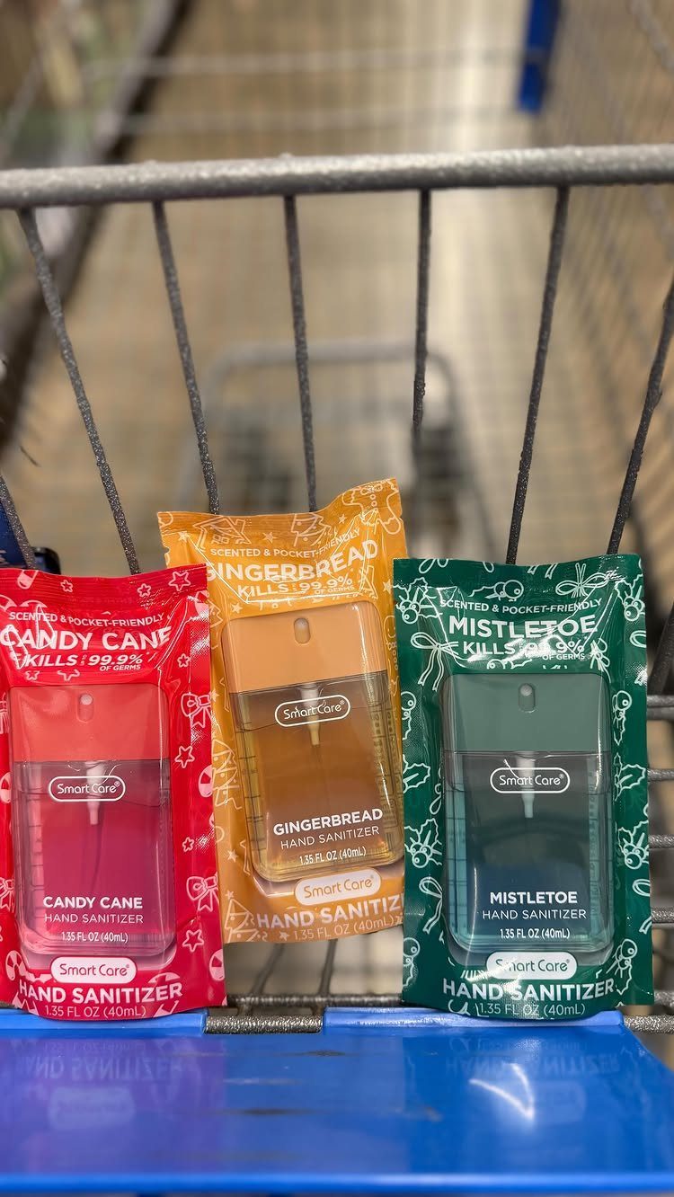 Three festive holiday-themed hand sanitizers sitting on a blue shopping cart edge.