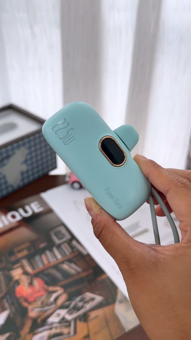 Light blue portable power bank held in a hand over a blurred background.