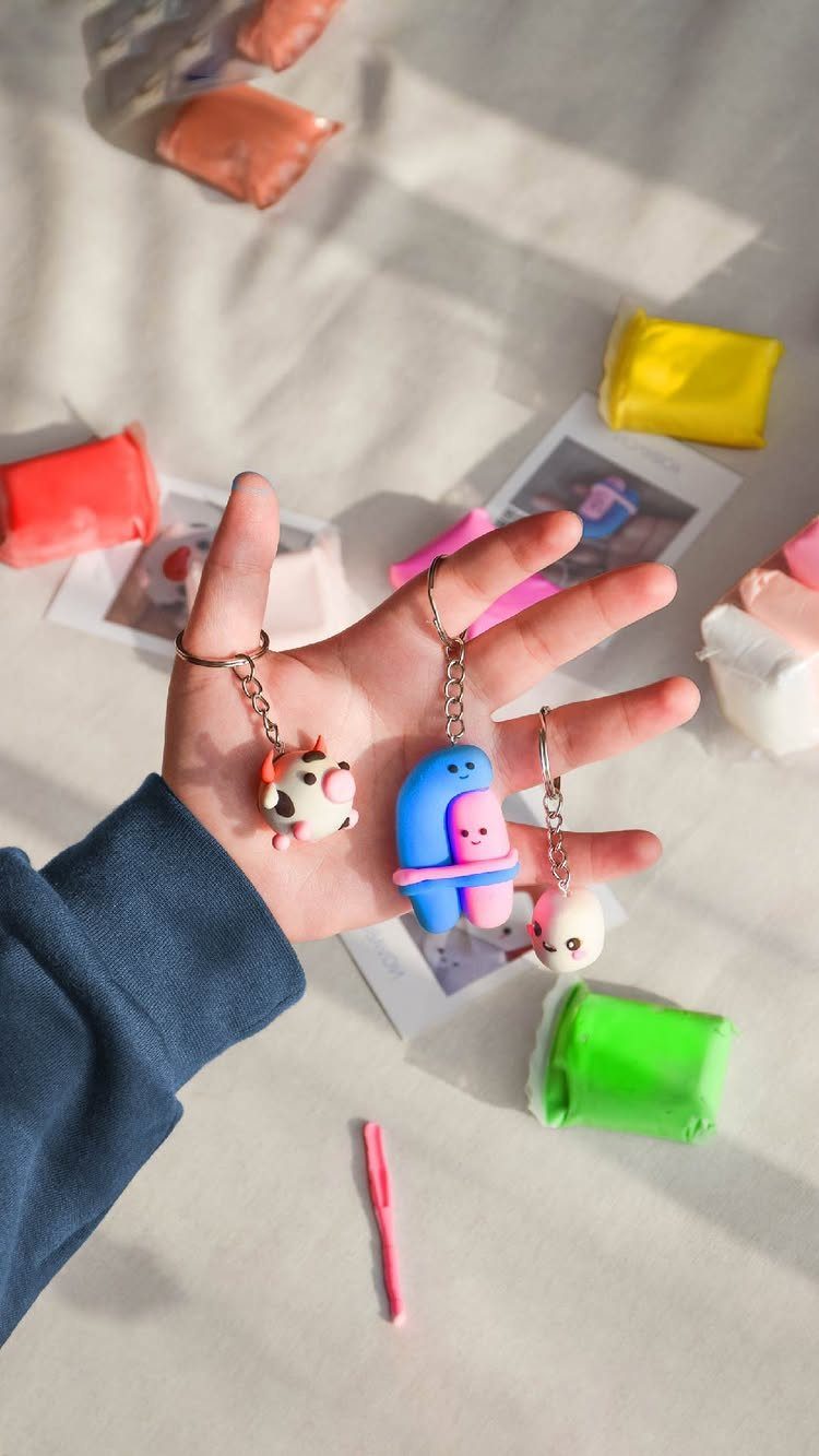 Hand holding colorful polymer clay character keychains surrounded by blocks of modeling clay.