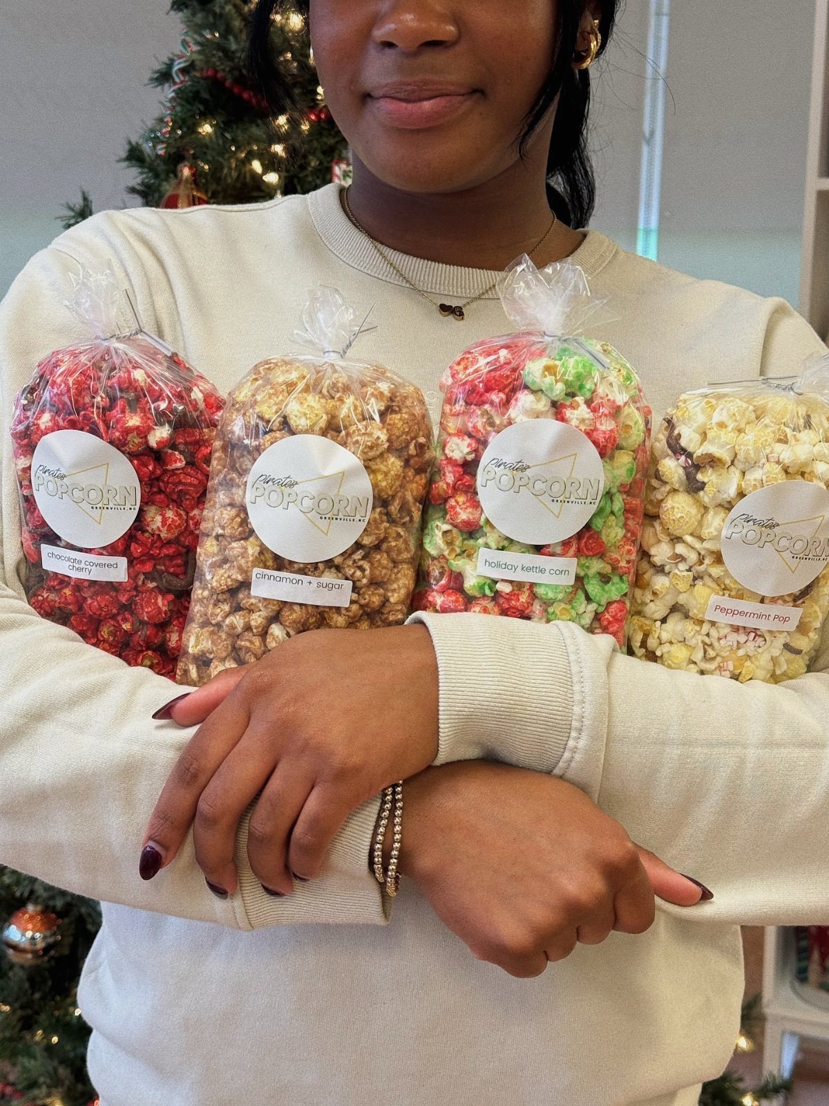 Four bags of colorful seasoned popcorn held by a person in a sweater.