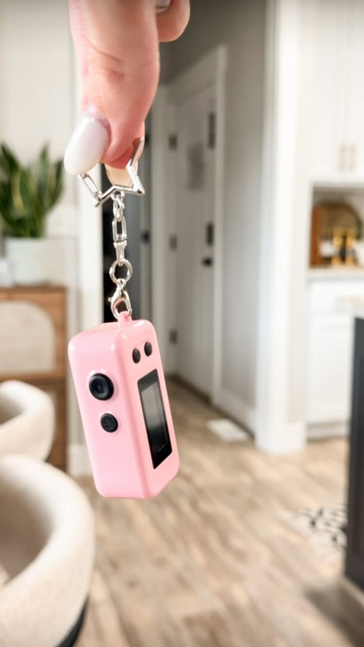 Small pink digital camera on a silver keychain held by a hand.