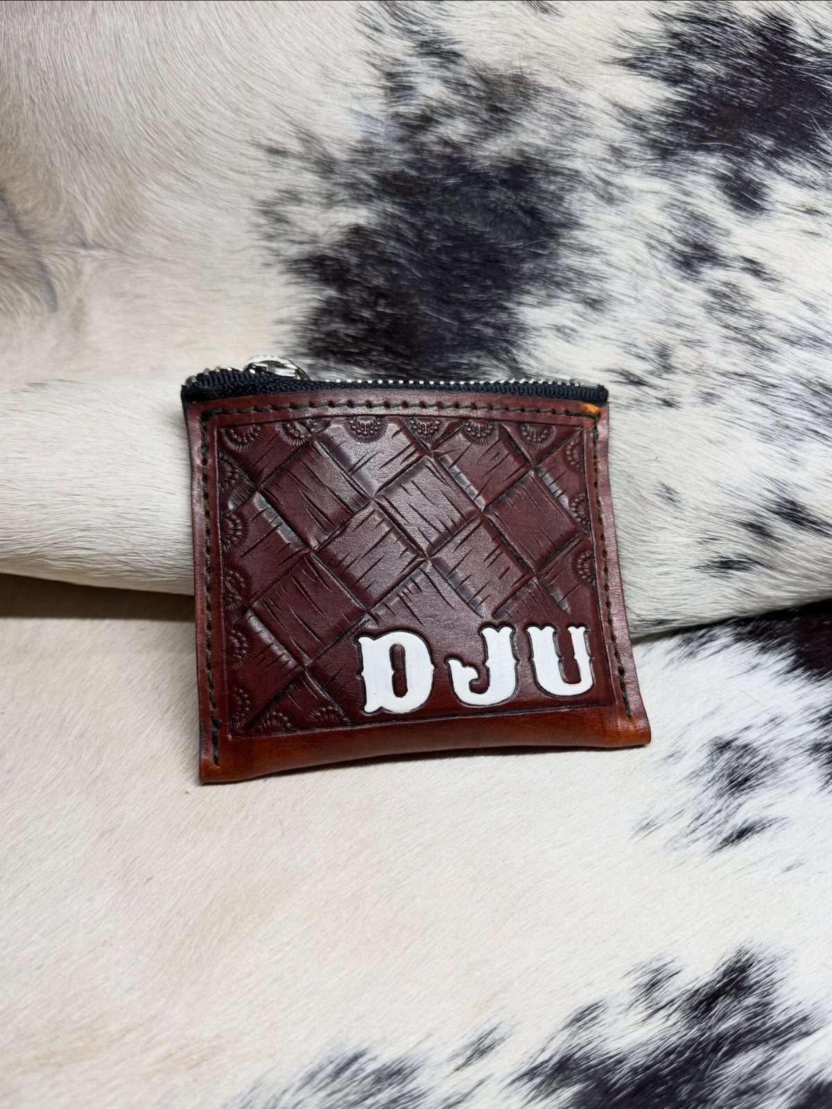 Brown leather zippered pouch with white initials on a cowhide background