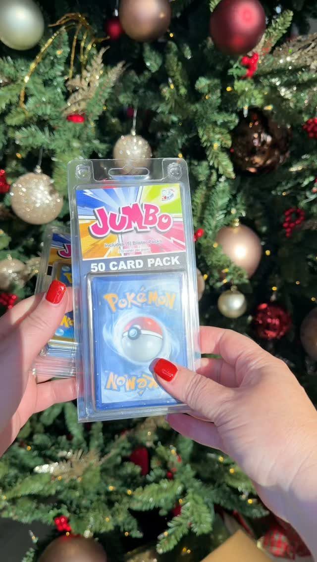 Hands holding a Pokemon card pack in front of a decorated Christmas tree.