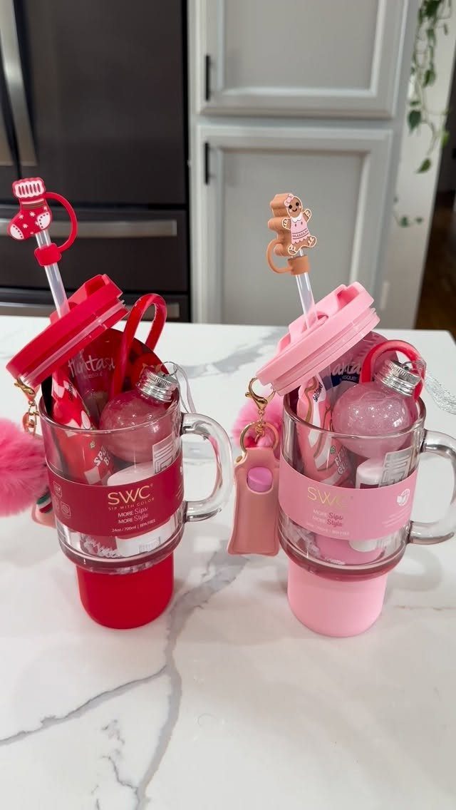 Two festive glass mugs filled with small beauty gifts on a marble counter.