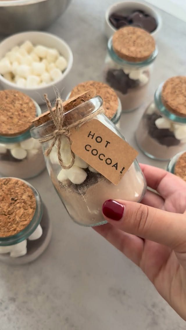 Glass jar filled with hot cocoa mix and marshmallows held by a hand.