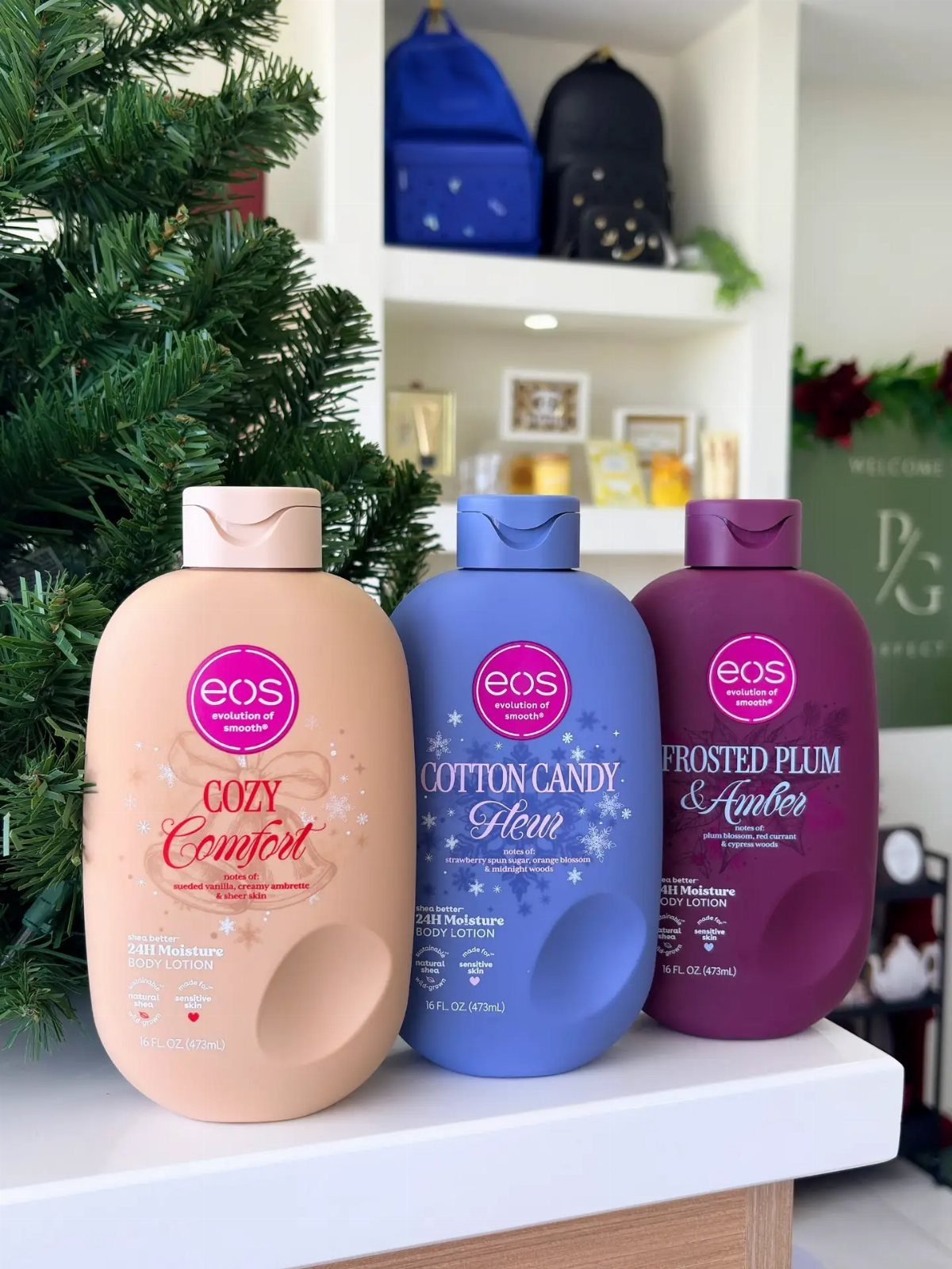 Three colorful bottles of eos body lotion next to a Christmas tree.