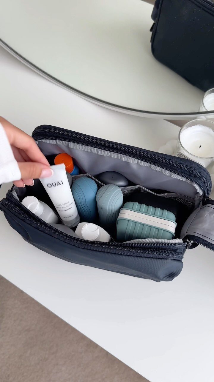 Small white beauty tube held over a navy toiletry bag filled with travel containers.