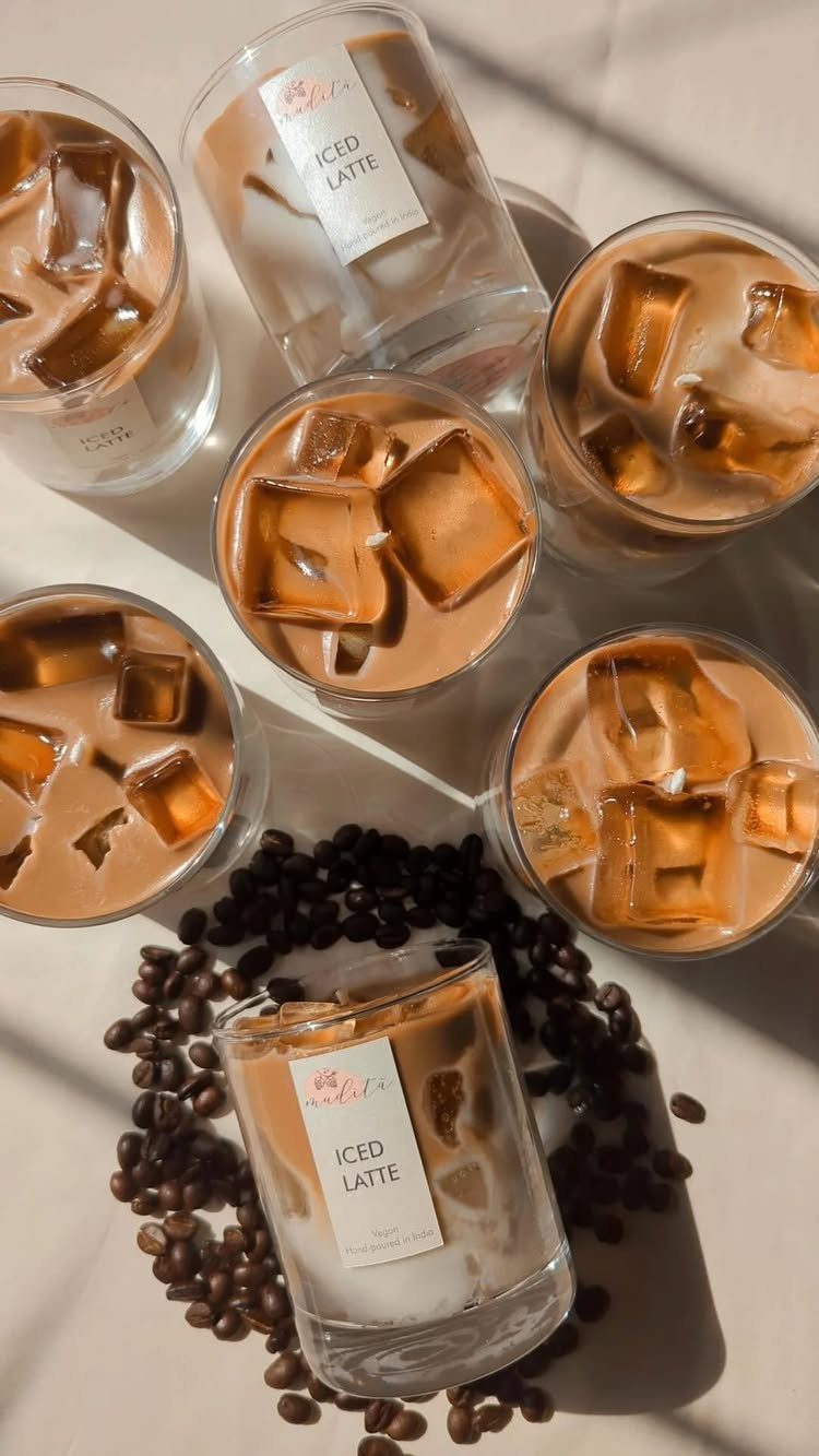 Coffee-scented candles resembling iced lattes surrounded by real iced coffee and coffee beans.