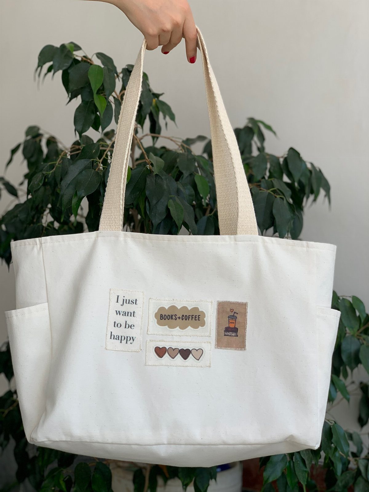 Cream canvas tote bag with coffee and book themed patches held by hand