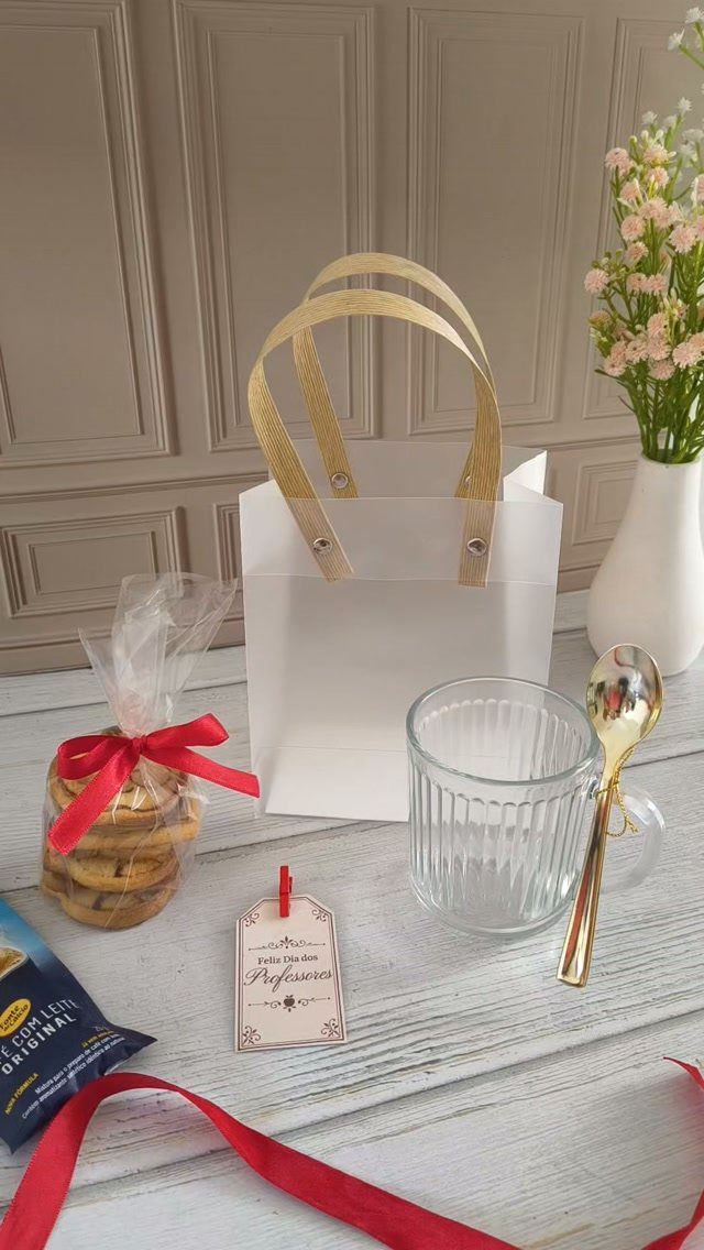Gift set with white bag, glass mug, gold spoon, and cookies on wood.