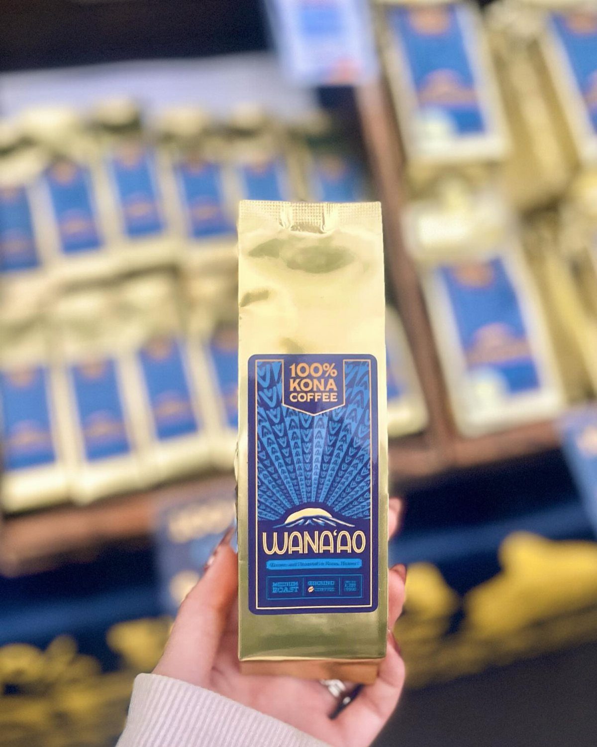 Gold foil bag of Kona coffee held in front of a store shelf.