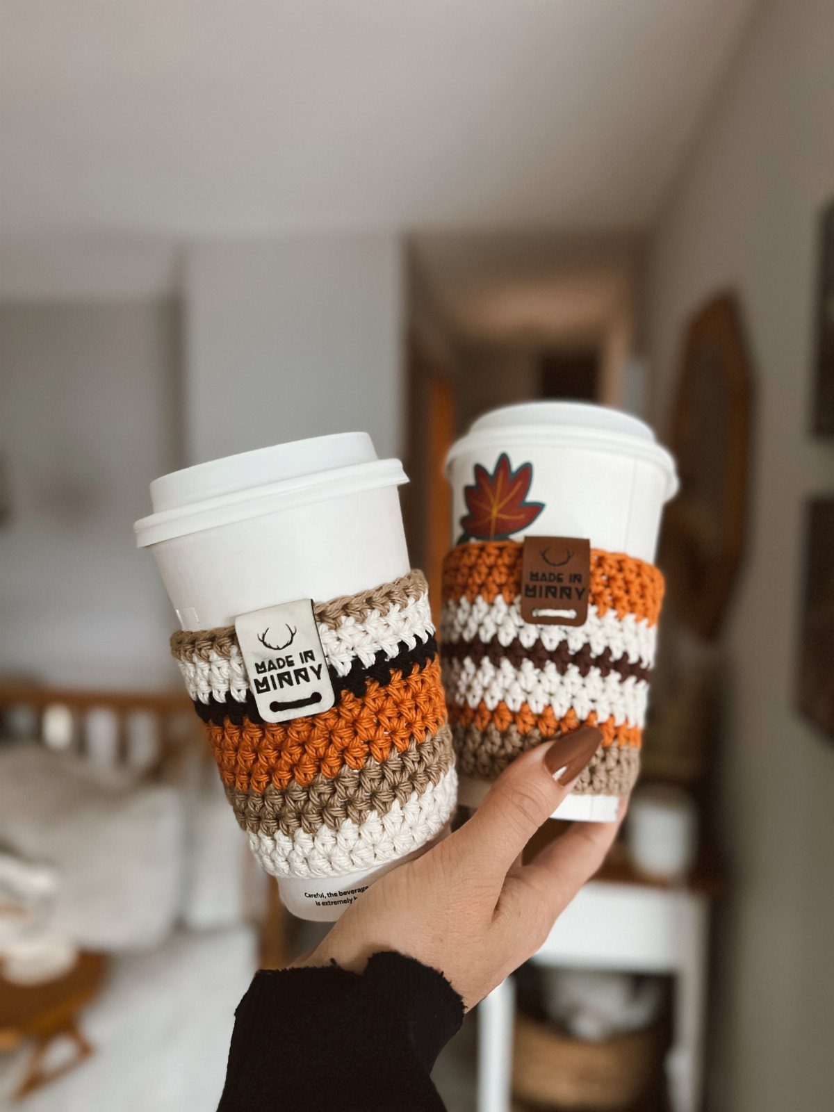 Two white coffee cups with orange and brown crocheted reusable cup sleeves.