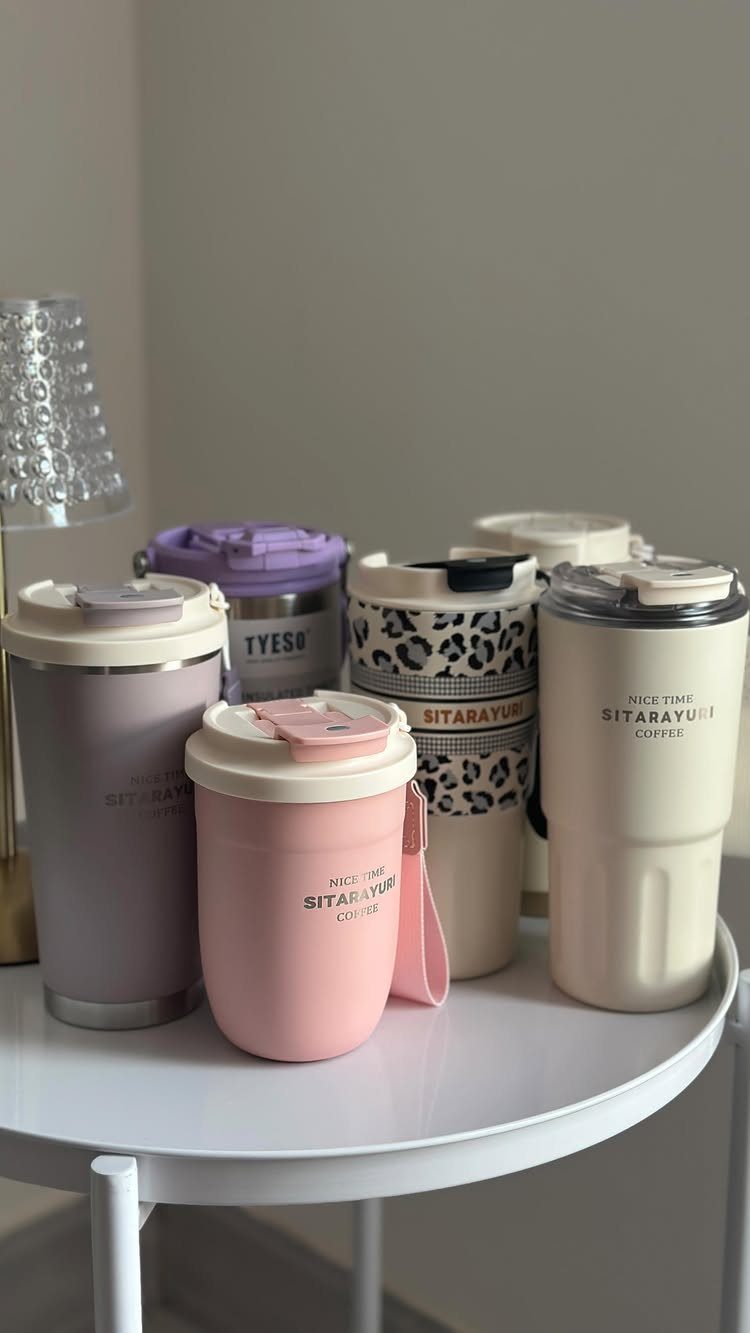 Assorted travel coffee tumblers in pastel colors and leopard print on a white table.