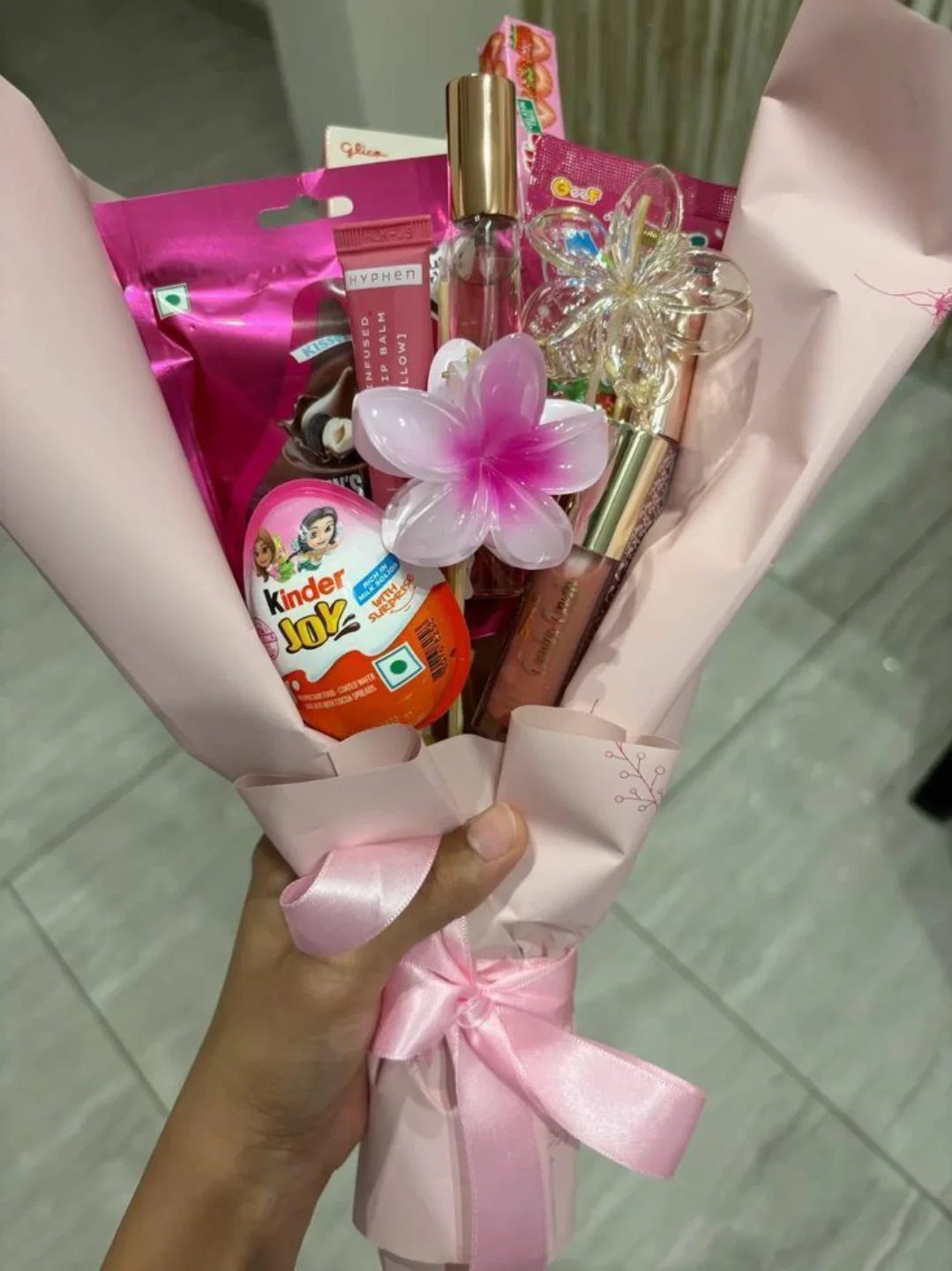 Gift bouquet wrapped in pink paper containing sweets, cosmetics, and a flower ornament.