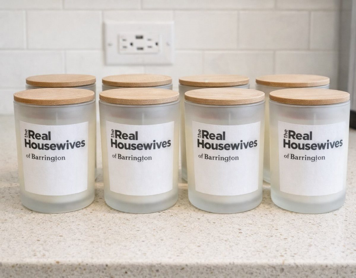 Eight frosted glass candles with wooden lids and personalized labels on a counter.