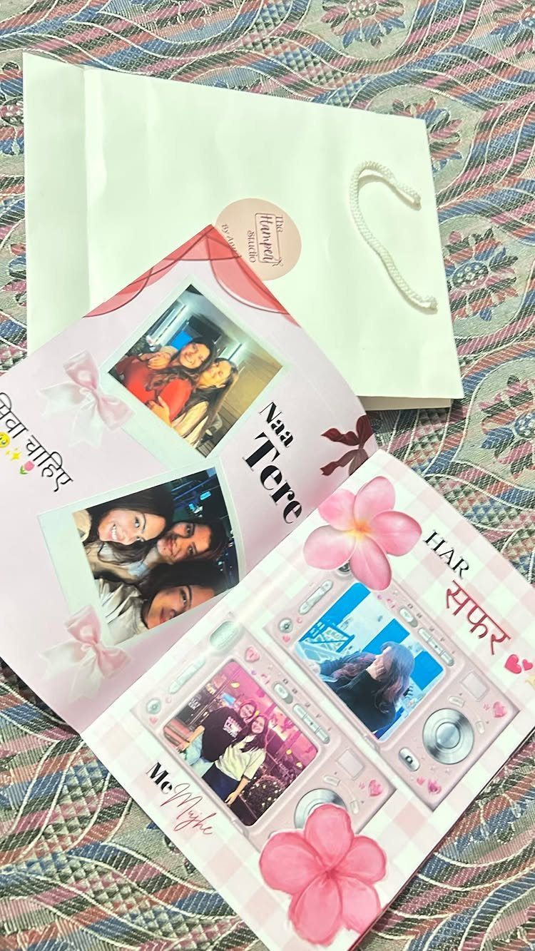Handmade scrapbook with photos of friends and pink flowers next to a white bag.