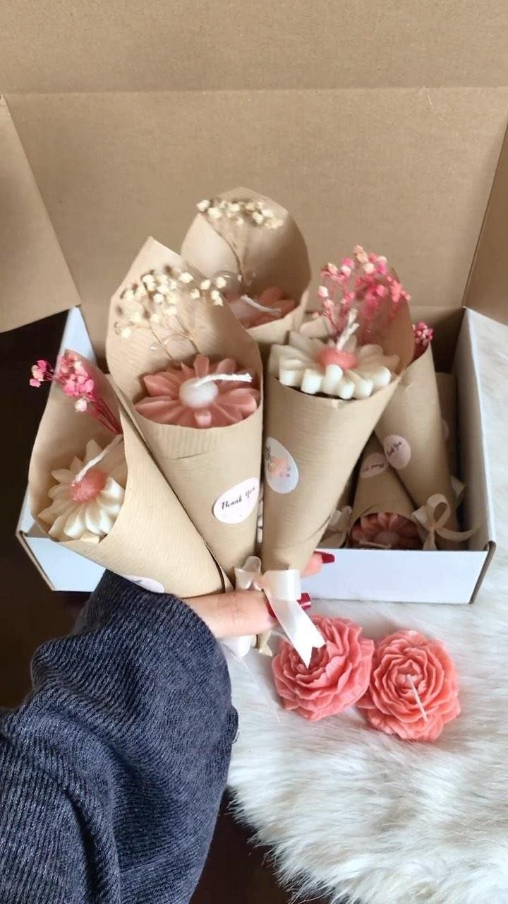 Flower-shaped candles wrapped in brown paper held over a white faux fur rug