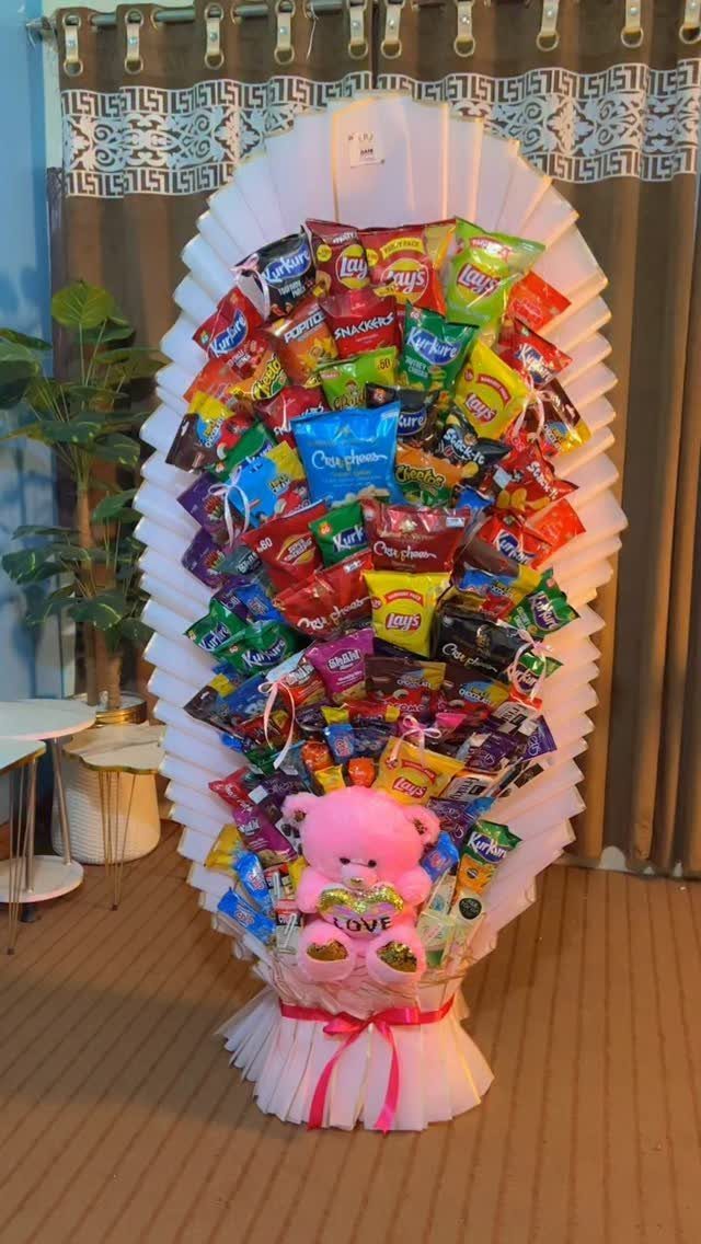 Fan-shaped snack bouquet with various colorful candy bags and a pink teddy bear.